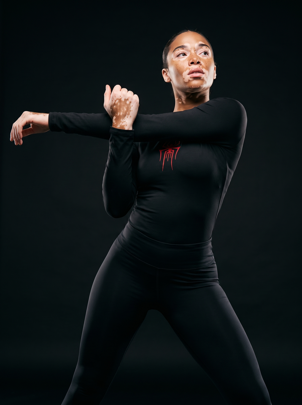 Athletic female model with vitiligo wearing Vagabane Arachnita hip-length spider print training top — studio campaign shot